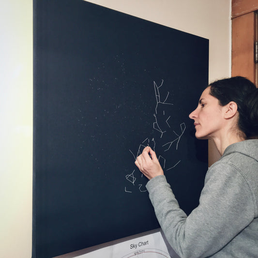 The artist working on a new 30" square embroidery with white thread on a navy canvas